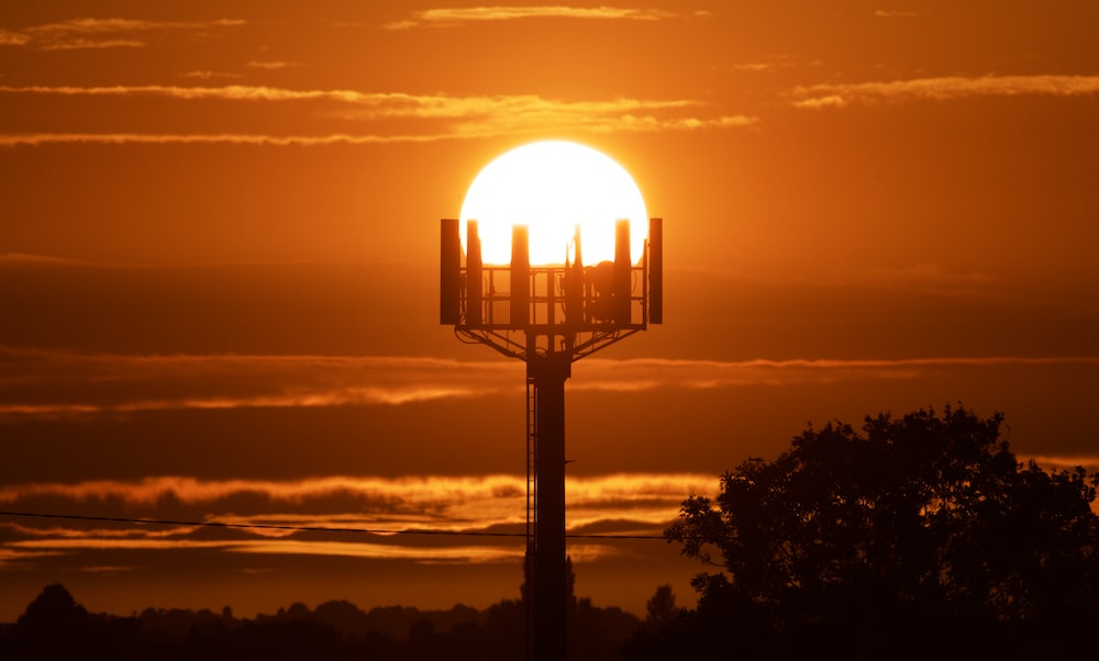 the sun is setting behind a tower with a cell phone on it