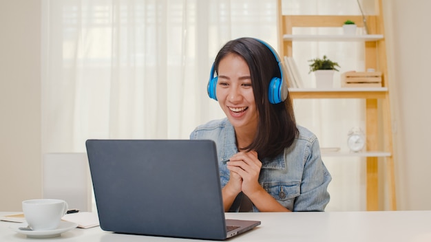 Free photo freelance business women casual wear using laptop working call video conference with customer in workplace in living room at home. happy young asian girl relax sitting on desk do job in internet.