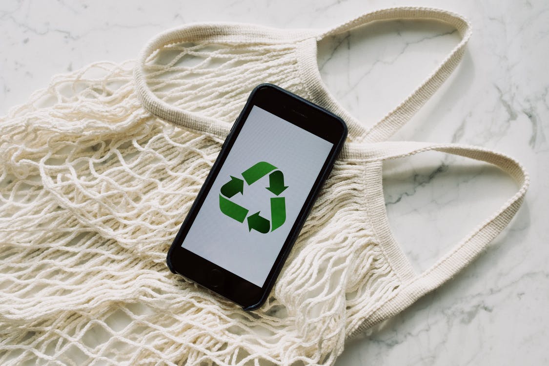 Smartphone with recycling sign on screen placed on white mesh bag on marble table