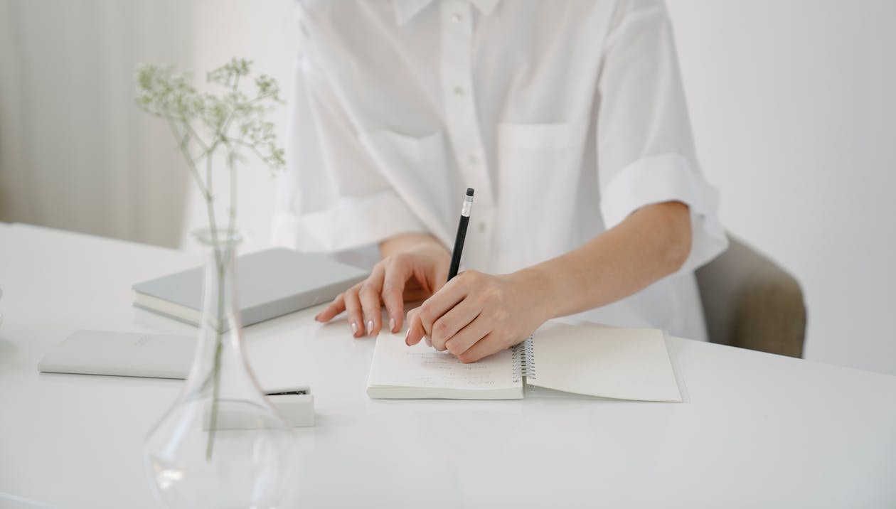 Crop person writing in notebook at table